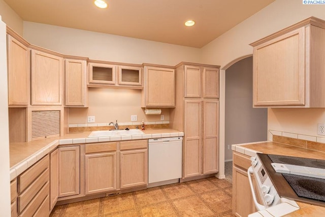 kitchen featuring white appliances, light brown cabinets, arched walkways, and a sink