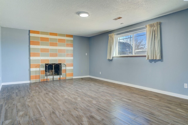 unfurnished living room with baseboards, visible vents, an accent wall, wood finished floors, and a fireplace