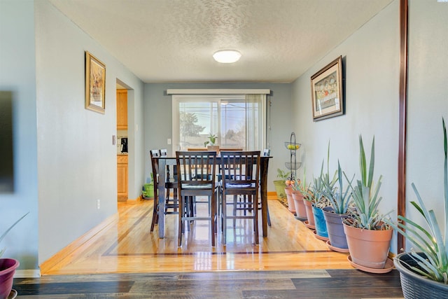 dining space with a textured ceiling, wood finished floors, and baseboards