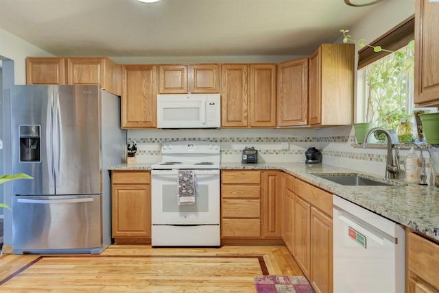 kitchen with light stone counters, backsplash, light wood-style flooring, a sink, and white appliances