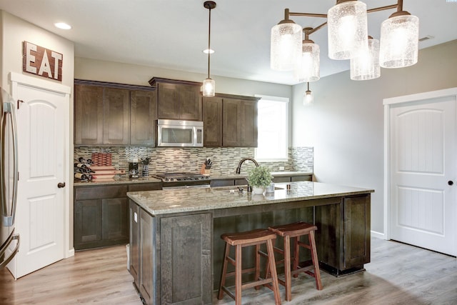 1390 Jade Ave, West Richland, WA 99353 - kitchen featuring stainless steel appliances, backsplash, light stone counters, dark brown cabinetry, and an island with sink