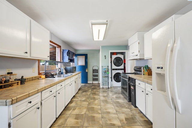 kitchen featuring stacked washer and dryer, stainless steel range with electric cooktop, tile countertops, white fridge with ice dispenser, and white cabinets