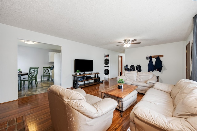 living room with hardwood / wood-style flooring, ceiling fan, stacked washer and clothes dryer, and a textured ceiling