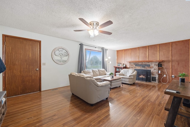 living room featuring wood-type flooring, ceiling fan, a textured ceiling, and a fireplace