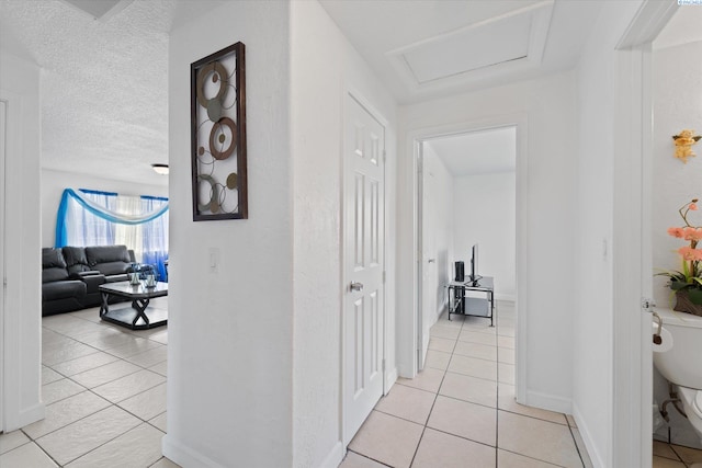 corridor with baseboards, attic access, and light tile patterned floors