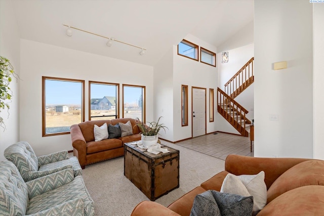 living room with rail lighting, light carpet, high vaulted ceiling, baseboards, and stairs