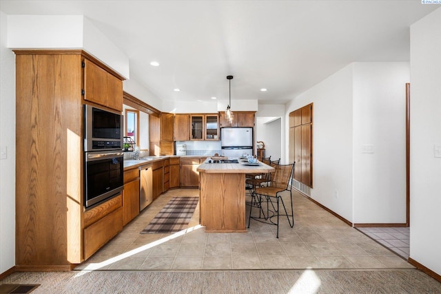 kitchen featuring a center island, a kitchen breakfast bar, light countertops, appliances with stainless steel finishes, and brown cabinets