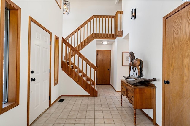 foyer entrance with visible vents, a towering ceiling, baseboards, and stairs