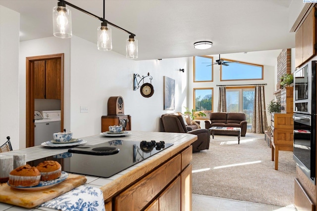 kitchen featuring light carpet, tile counters, vaulted ceiling, washer and dryer, and stainless steel oven