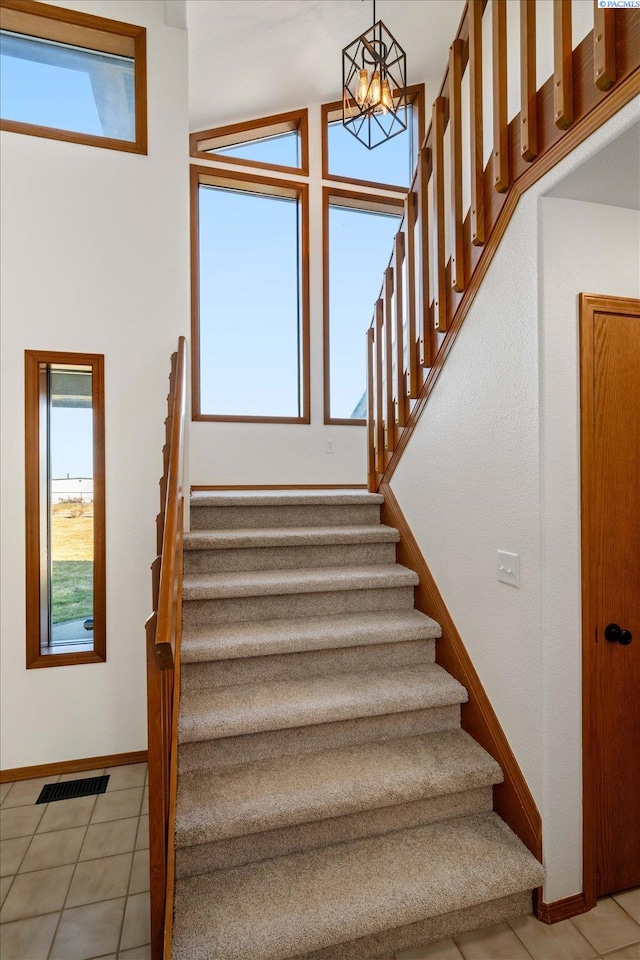 stairway with baseboards, tile patterned flooring, visible vents, and a notable chandelier