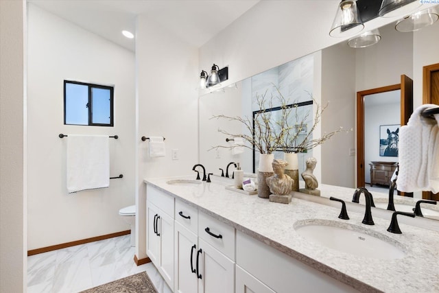 full bath featuring toilet, marble finish floor, double vanity, and a sink