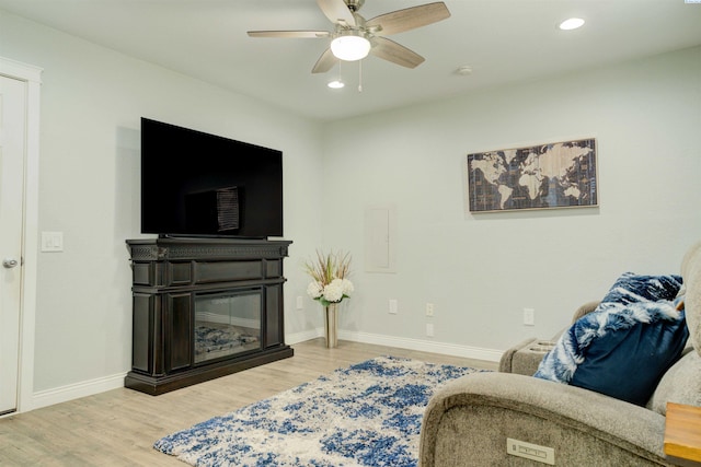 living room featuring wood finished floors, a glass covered fireplace, recessed lighting, baseboards, and ceiling fan