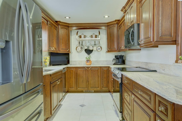 kitchen featuring light tile patterned floors, light stone counters, brown cabinetry, and appliances with stainless steel finishes