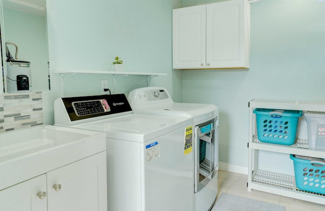 laundry area with baseboards, washer and clothes dryer, light tile patterned floors, water heater, and cabinet space