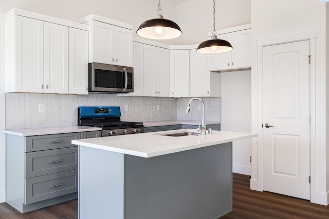 kitchen featuring white cabinets, an island with sink, appliances with stainless steel finishes, decorative light fixtures, and a sink