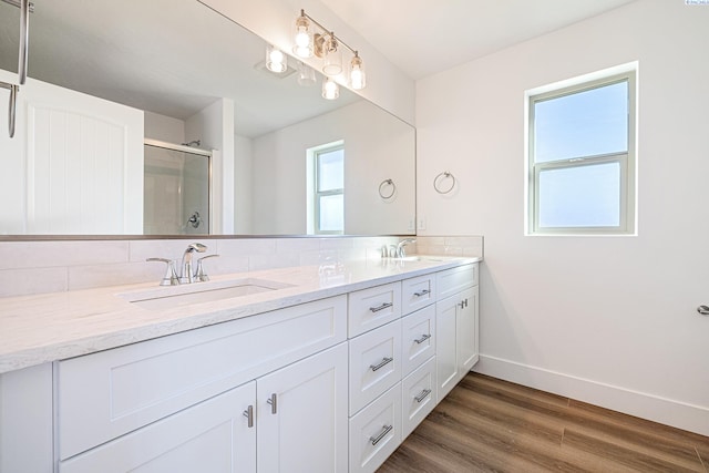 full bath with double vanity, a sink, baseboards, and wood finished floors