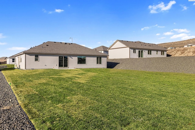 rear view of property featuring a shingled roof, fence, and a yard