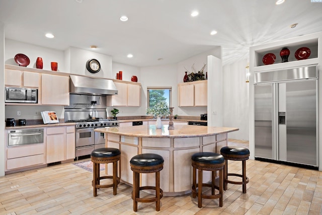 kitchen featuring light brown cabinetry, extractor fan, a breakfast bar area, high end appliances, and a kitchen island