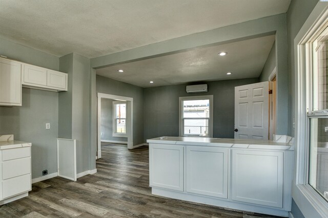 503 Grandridge Ave, Grandview, WA 98930 - kitchen featuring a wall mounted AC, baseboards, a peninsula, white cabinetry, and dark wood finished floors
