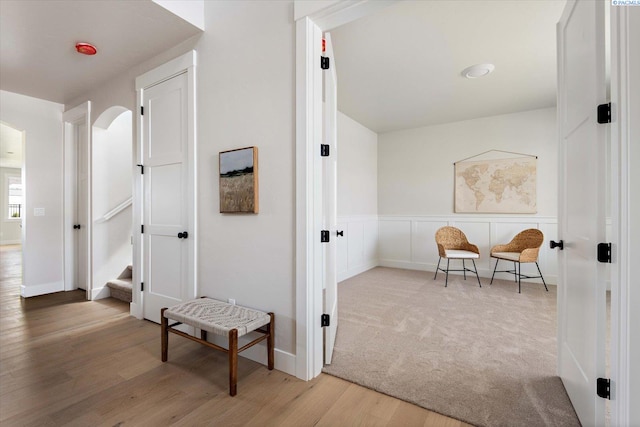 hall featuring arched walkways, carpet, wood finished floors, and a decorative wall