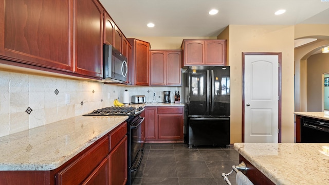 kitchen with black appliances, arched walkways, light stone counters, and decorative backsplash