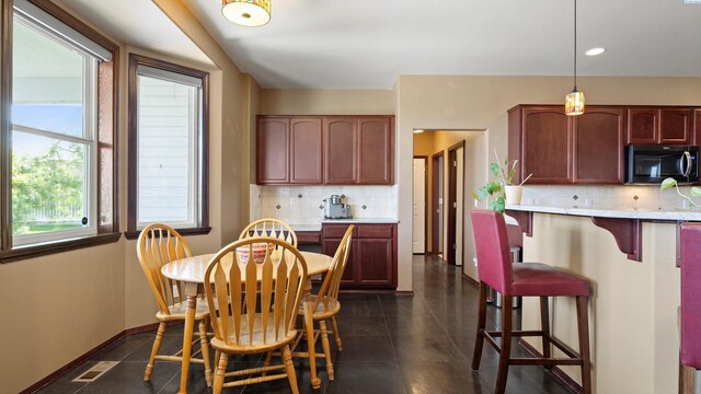 kitchen featuring a kitchen bar, tasteful backsplash, visible vents, hanging light fixtures, and dark tile patterned floors