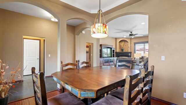 dining area featuring wood-type flooring, arched walkways, ceiling fan, and baseboards