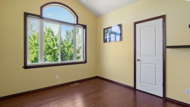 empty room featuring dark wood-style floors, visible vents, vaulted ceiling, and a healthy amount of sunlight