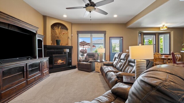 living room featuring recessed lighting, light carpet, a warm lit fireplace, and ceiling fan