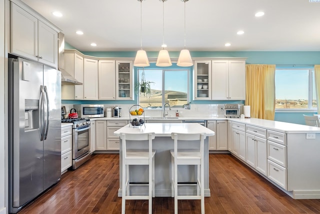 kitchen featuring stainless steel appliances, light countertops, glass insert cabinets, a sink, and a peninsula