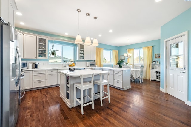 kitchen with a peninsula, dark wood-style flooring, a kitchen island, white cabinetry, and appliances with stainless steel finishes