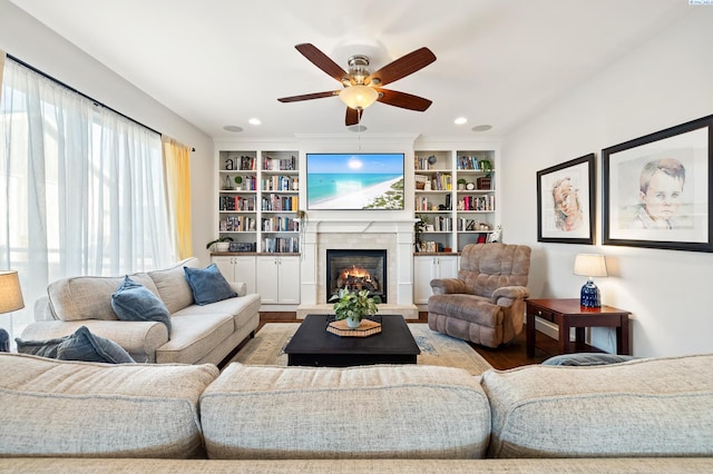 living area featuring built in features, recessed lighting, a ceiling fan, wood finished floors, and a lit fireplace