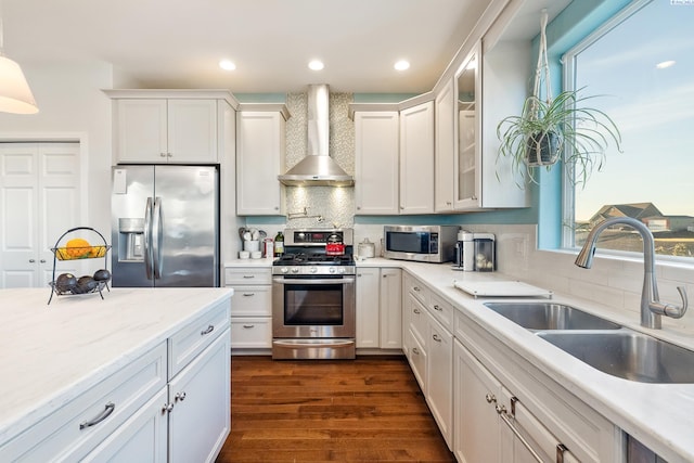 kitchen with a sink, white cabinets, appliances with stainless steel finishes, wall chimney range hood, and dark wood finished floors