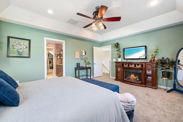 bedroom featuring a warm lit fireplace, visible vents, baseboards, a tray ceiling, and carpet