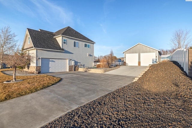 view of side of home featuring a garage, an outdoor structure, fence, stone siding, and roof with shingles