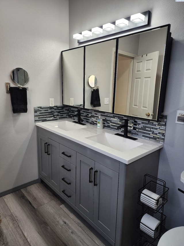 full bath featuring double vanity, decorative backsplash, a sink, and wood finished floors