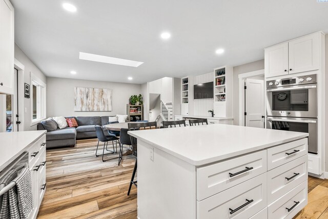 kitchen with a center island, a skylight, light hardwood / wood-style flooring, stainless steel double oven, and white cabinets