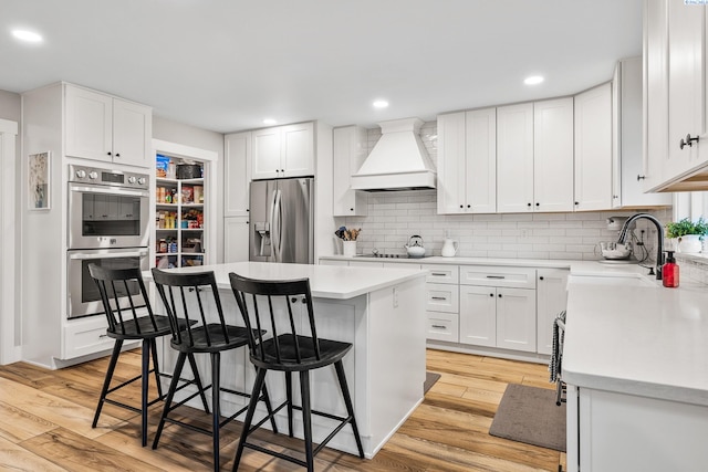 kitchen with a breakfast bar area, custom exhaust hood, white cabinetry, a kitchen island, and stainless steel appliances