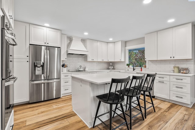 kitchen with a breakfast bar, white cabinets, a kitchen island, stainless steel fridge with ice dispenser, and custom exhaust hood