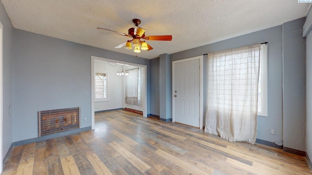 unfurnished living room featuring heating unit, wood-type flooring, a textured ceiling, a fireplace, and ceiling fan with notable chandelier