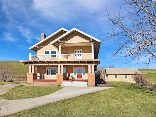 rear view of house featuring a balcony, covered porch, and a lawn