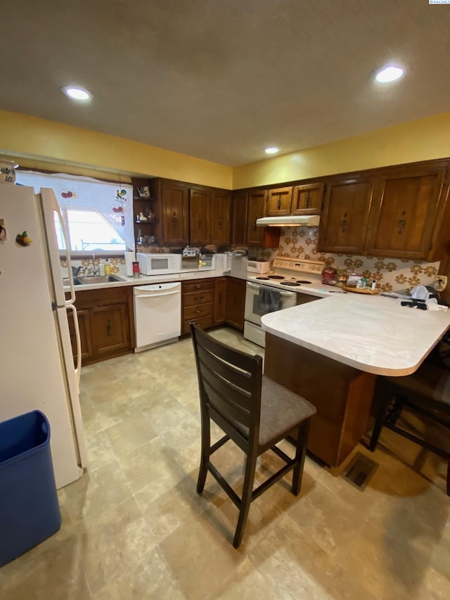 kitchen with under cabinet range hood, a peninsula, white appliances, a breakfast bar, and light countertops