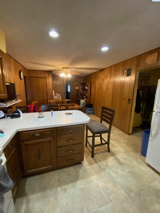 kitchen with ceiling fan, brown cabinets, freestanding refrigerator, a peninsula, and light countertops