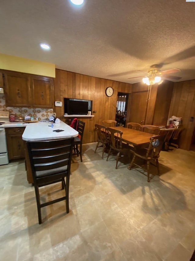 dining space featuring wood walls, a textured ceiling, and a ceiling fan