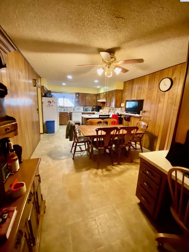 dining room featuring a textured ceiling, wooden walls, and a ceiling fan