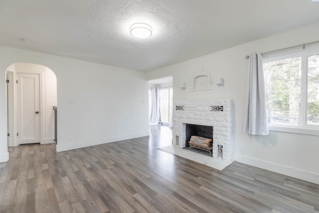 615 SW Winter Cir, Pullman, WA 99163 - unfurnished living room featuring arched walkways, a stone fireplace, wood finished floors, baseboards, and a textured ceiling