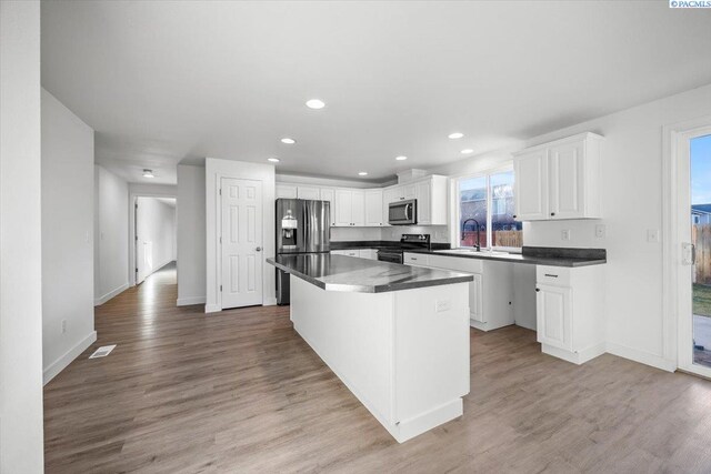 kitchen featuring a breakfast bar, appliances with stainless steel finishes, white cabinetry, light hardwood / wood-style floors, and a kitchen island