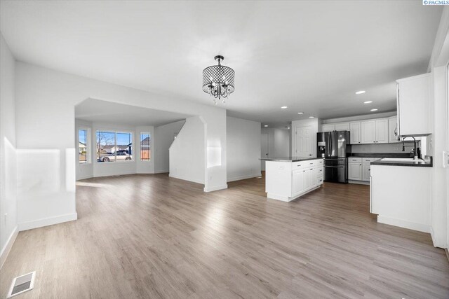 kitchen with pendant lighting, white cabinetry, a notable chandelier, black fridge, and light hardwood / wood-style flooring