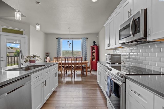 kitchen featuring appliances with stainless steel finishes, a sink, backsplash, light wood-type flooring, and white cabinets