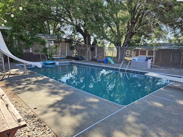 view of pool with a water slide, a diving board, and a patio